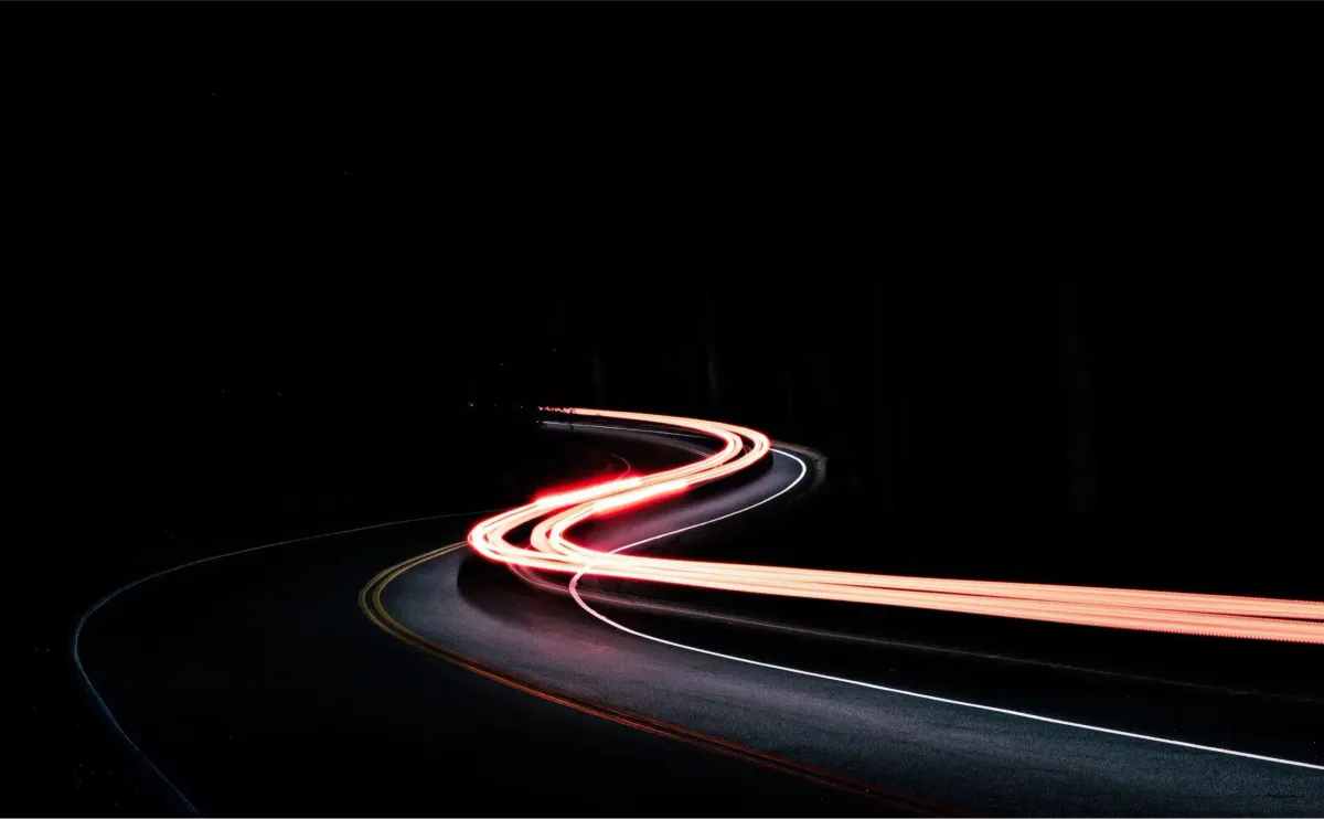 Long-exposure light trails curving along a dark road at night